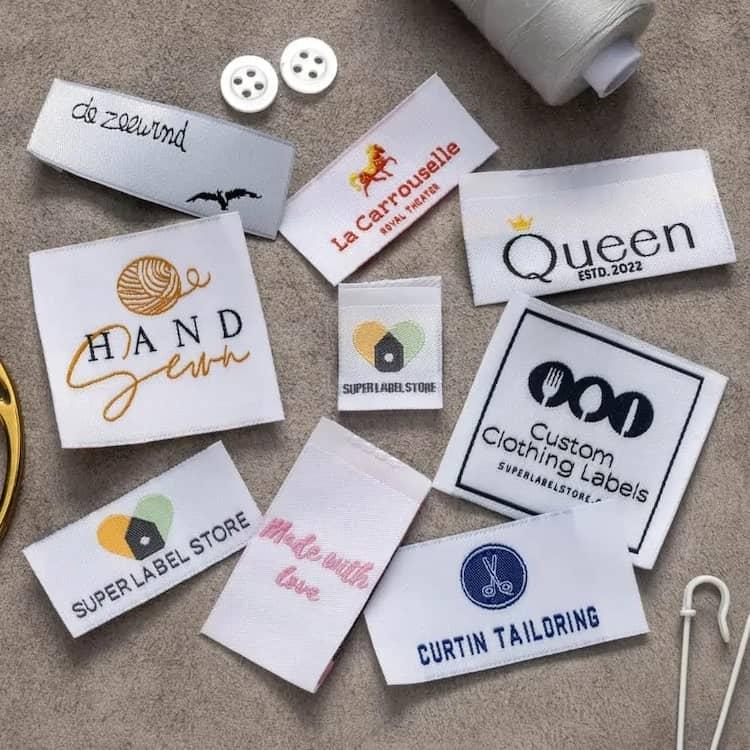 Assorted custom woven clothing labels, buttons, and thread spool on grey felt for apparel branding.